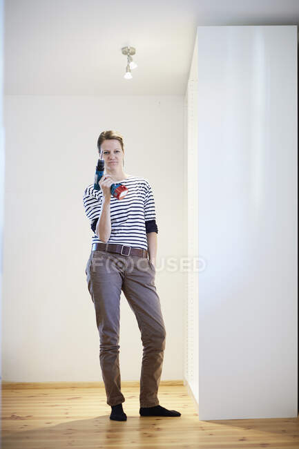 Portrait of mature woman holding up cordless screwdriver next to finished closet — Stock Photo