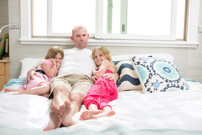 Portrait of mature man between two daughters on bed — Stock Photo