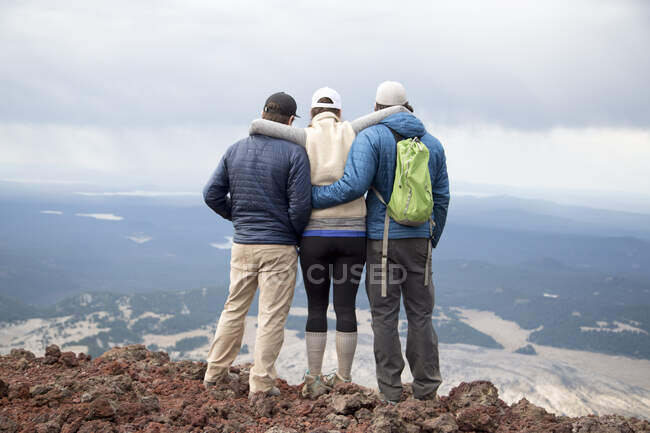 Tres amigos de pie en la cumbre del volcán South Sister, mirando a la vista, Bend, Oregon, EE.UU. - foto de stock