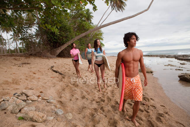Four young friends carrying surfboards on beach — Stock Photo