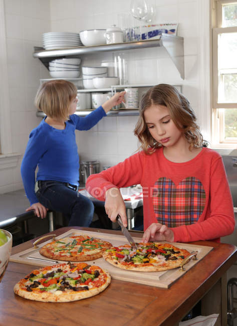 Zwei junge Mädchen in der Küche, die Pizza aufschneiden — Stockfoto