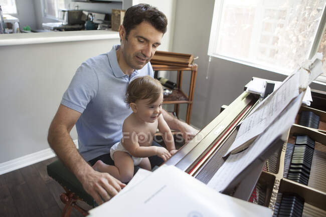 Niño sentado en la rodilla de los padres tocando el piano - foto de stock