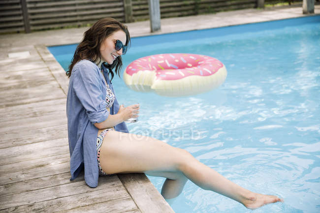 Mujer sentada junto a la piscina salpicando agua con los pies, Amagansett, Nueva York, Estados Unidos - foto de stock