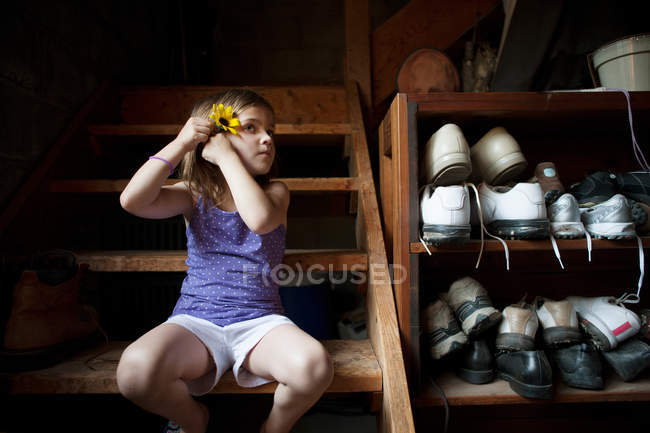 Little girl on basement steps, putting a flower in her hair — Stock Photo
