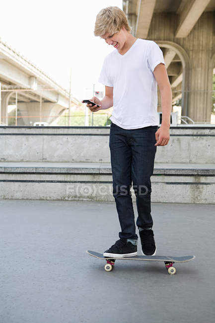 Хлопчик-підліток на скейті з мобільним телефоном — стокове фото