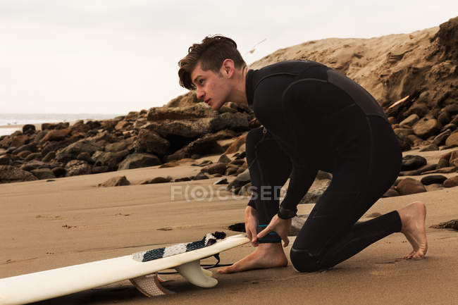 Jovem na praia com prancha, se preparando para surfar — Fotografia de Stock