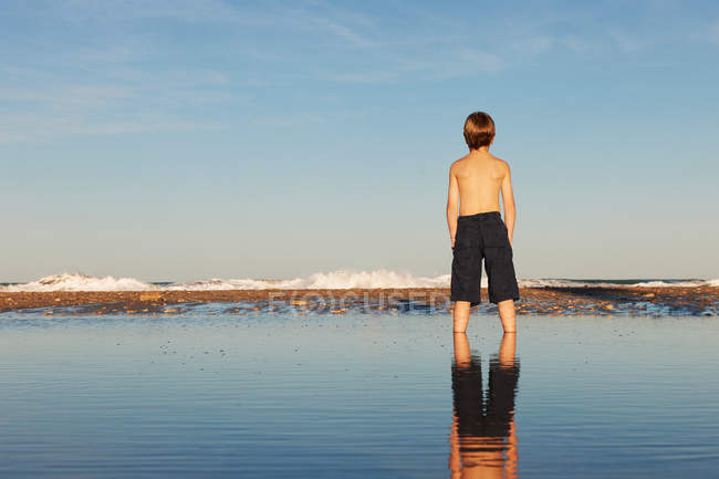 Rear view of boy and reflection standing on beach — Stock Photo