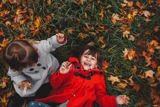 Overhead portrait of girl and toddler sister lying on grass and autumn leaves — Stock Photo