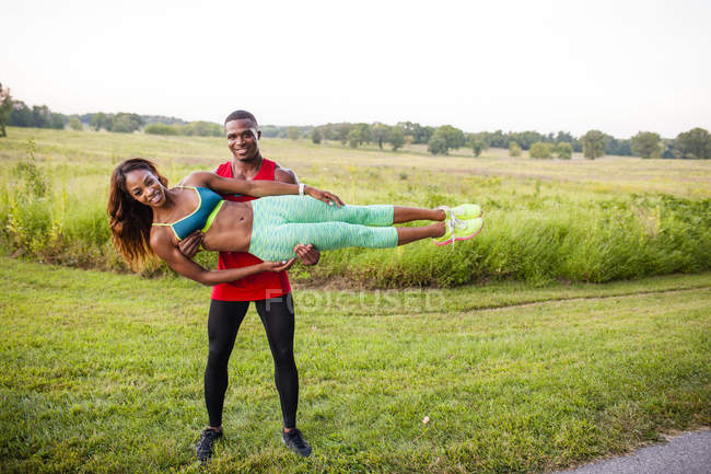 Young man training holding up girlfriend horizontally — Stock Photo