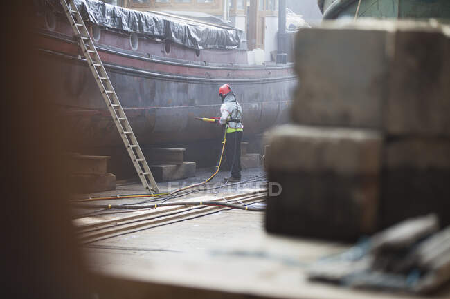 Trabajador arenado barco en astillero - foto de stock