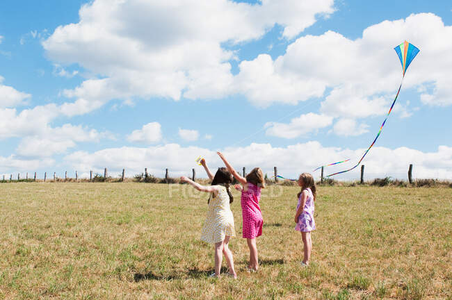 Tres chicas volando cometa en el campo - foto de stock