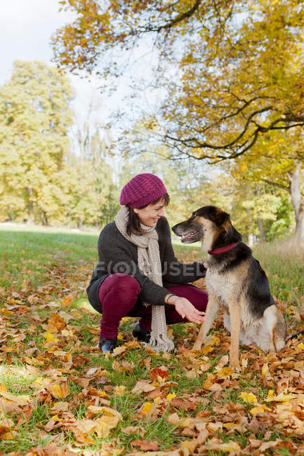 Donna sorridente che accarezza il cane nel parco in autunno — Foto stock