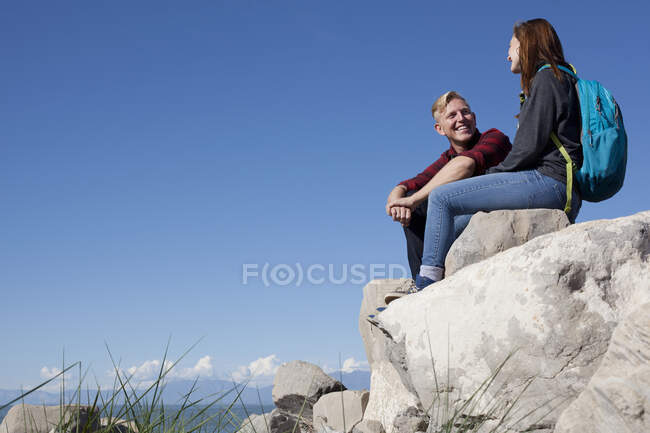 Vue à angle bas du jeune couple assis sur des rochers souriant — Photo de stock
