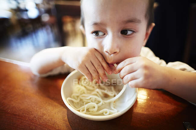 Niño comiendo fideos en el restaurante - foto de stock
