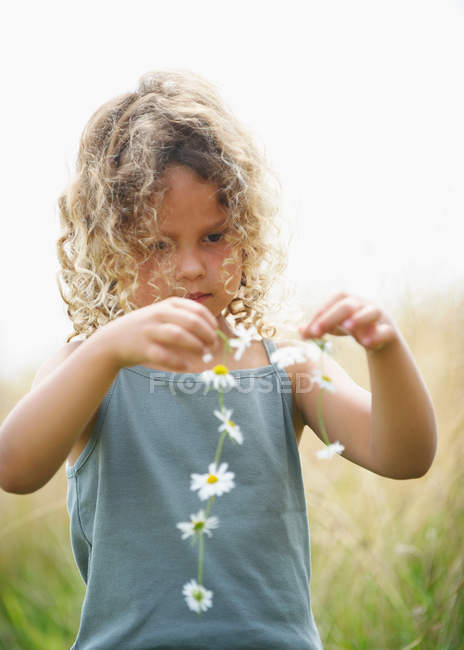 Jeune fille faisant une chaîne de marguerite — Photo de stock