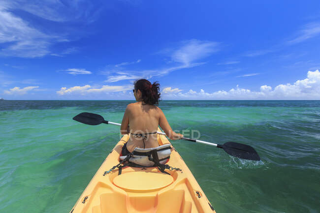 Rear view of woman sea kayaking, St. Georges Caye, Belize, Central America — стоковое фото