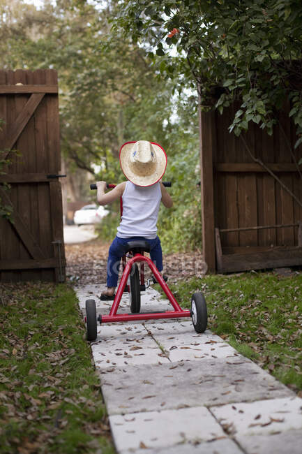 Чотирирічна дівчина їде на своєму триколісному велосипеді з садових воріт — стокове фото