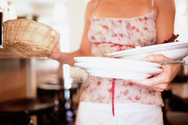 Camarera llevando canasta de mimbre y platos, recortados - foto de stock