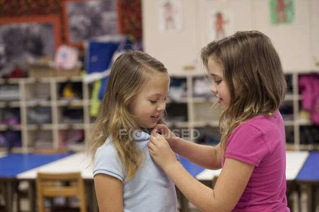 Girl buttoning friend's tee shirt in classroom — Stock Photo