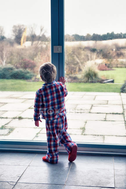 Ragazzo in pigiama guardando fuori dalla finestra — Foto stock