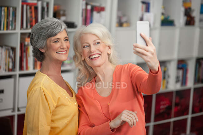 Two mature woman taking self portrait, using smartphone, indoors — Stock Photo