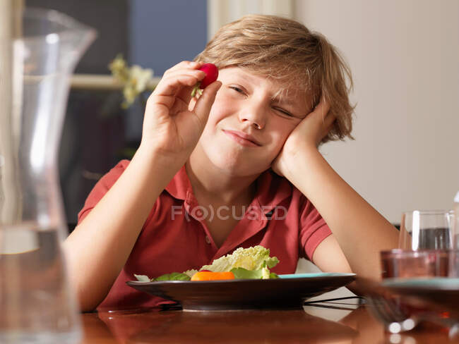 Junge schaut sich Rettich am Tisch genau an — Stockfoto