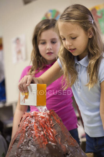 Girls with volcano model in classroom — Stock Photo