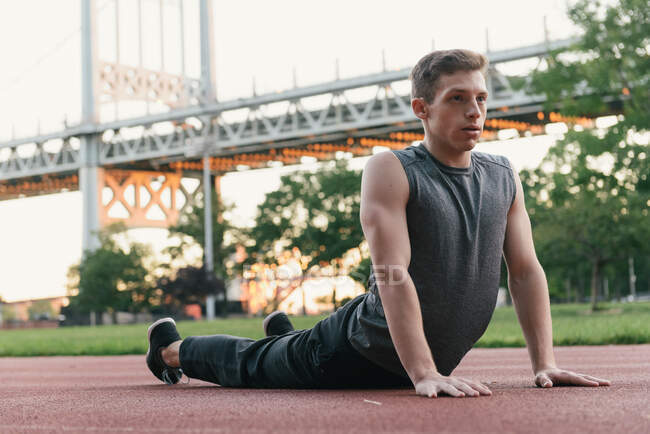 Young man on sports track, stretching — Stock Photo
