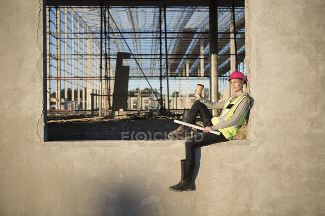 Arquitecta sentada en marco de ventana en obra - foto de stock