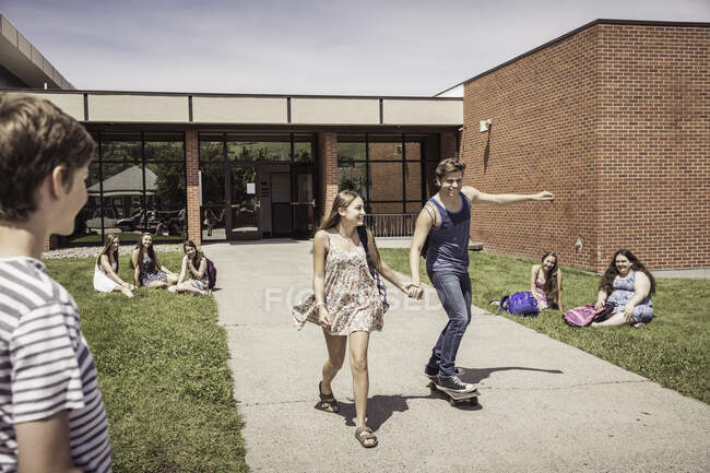 Adolescente casal do ensino médio skate enquanto deixa a escola — Fotografia de Stock