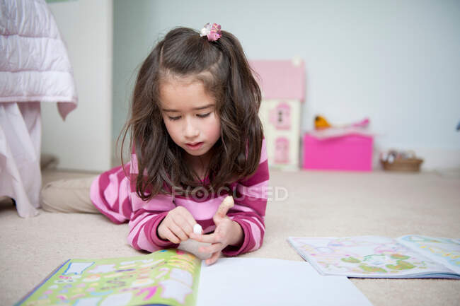 Girl lying on front and reading sticker book — Stock Photo