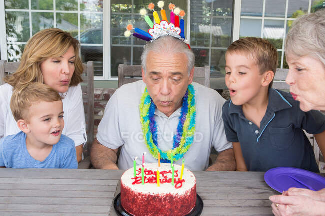 Uomo anziano che spegne candele sulla torta di compleanno con la famiglia — Foto stock