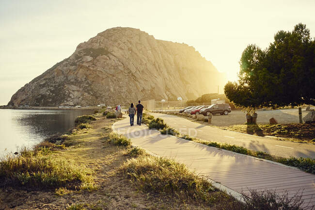 Pareja de turistas paseando hacia Morro Bay Rock, Morro Bay, California, Estados Unidos - foto de stock