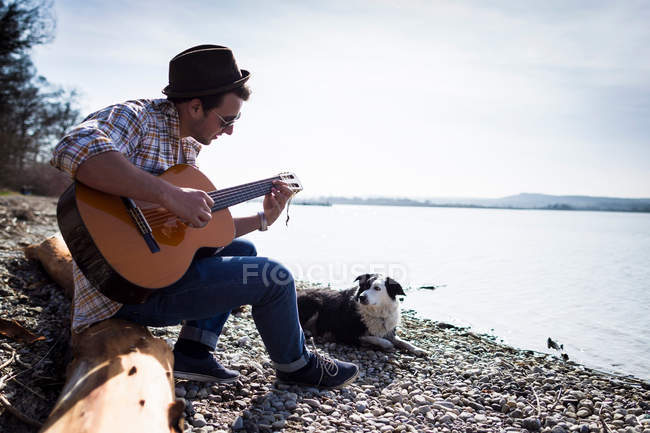 Homme jouant de la guitare avec chien par crique — Photo de stock