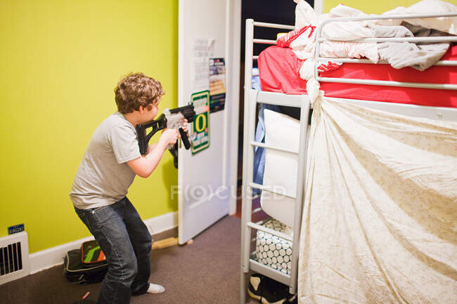 Мальчик играет с игрушечным пистолетом в спальне — стоковое фото