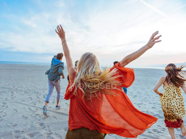 Gruppo di amici che camminano lungo la spiaggia, giovane donna con le braccia in aria, vista posteriore — Foto stock