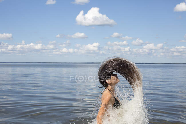 Mujer joven salpicando y arrojando hacia atrás el pelo largo del mar, Santa Rosa Beach, Florida, EE.UU. - foto de stock
