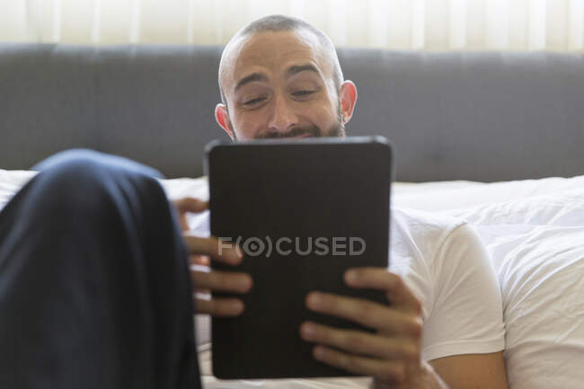 Mittlerer erwachsener Mann lehnt sich ans Bett und surft mit digitalem Tablet — Stockfoto