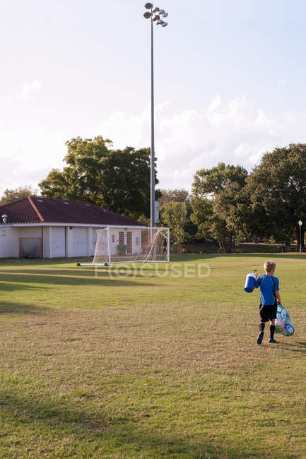 Вид спереду хлопчика футболіста, який несе сумку з футболу на полі тренування — стокове фото