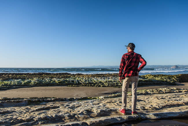 Молодий чоловік стоїть на пляжі, дивлячись на океан, вид ззаду — стокове фото