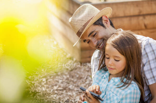 Девушка на коленях отцов с помощью смартфона в общественном саду — стоковое фото