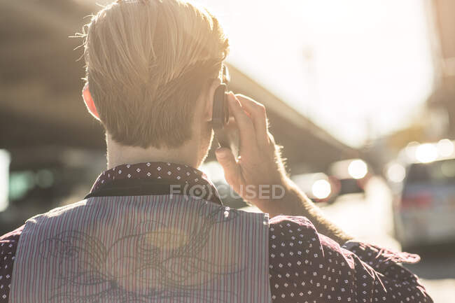 Vista posteriore del giovane uomo d'affari che parla su smartphone sulla strada della città — Foto stock