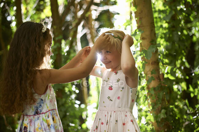 Two girls putting on tiaras in sunlit forest — Stock Photo