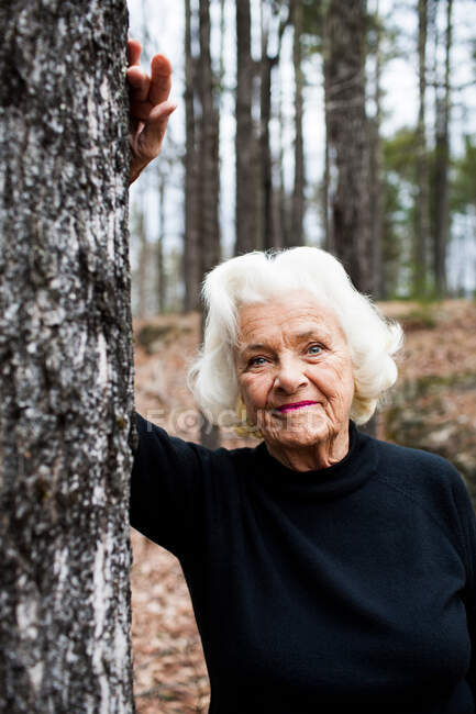 Retrato de mulher idosa apoiada em tronco de árvore na floresta — Fotografia de Stock