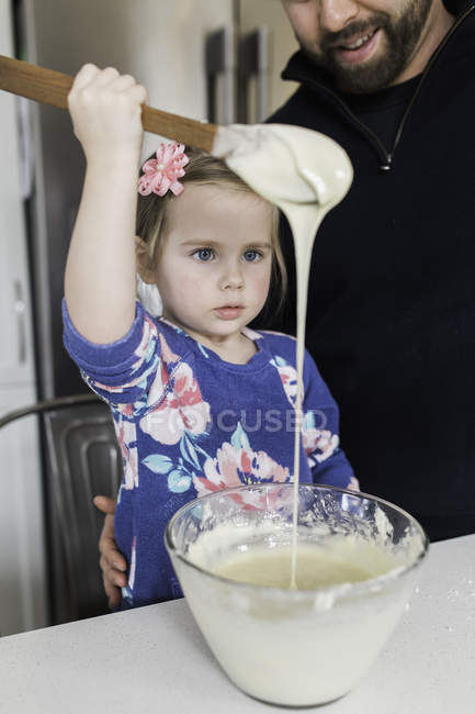 Girl with father gazing at wooden spoon drizzle at kitchen counter — Stock Photo