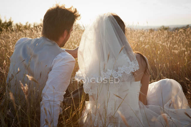 Newlywed couple sitting in tall grass — Stock Photo