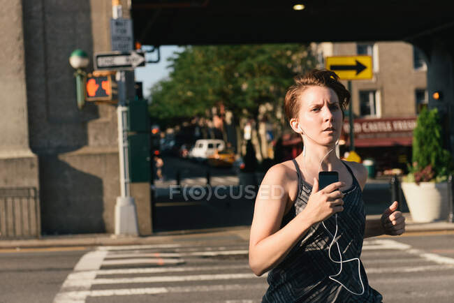 Mujer adulta, corriendo, usando auriculares, al aire libre - foto de stock