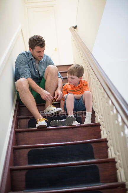 Padre e hijo sentados en escaleras atando cordones - foto de stock