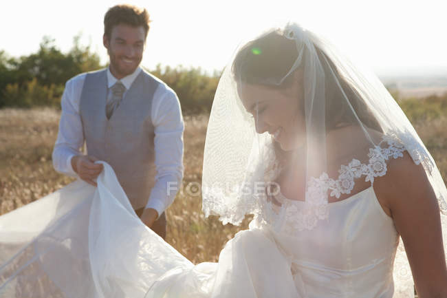 Newlywed groom holding brides dress — Stock Photo