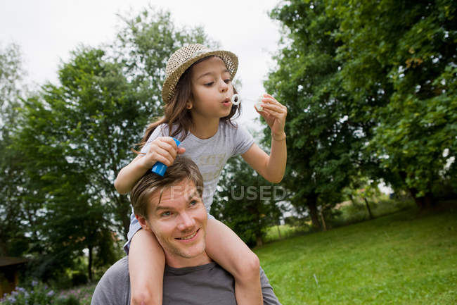 Дівчина з бульбашками на плечах батьків — стокове фото